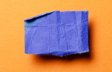 Fototapeta premium One single blue torn ripped wrinkled crumpled blank paper note with drop shadow, folded edge and copy space for text on orange background