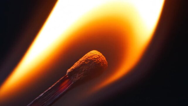 Macro shot of burning matchstick with bright orange flame against dark background