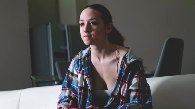 Portrait of a teenage girl playing video games on a white sofa at home at night