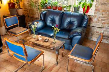 A sweet and warm corner of a cafe with leather armchairs, many plants, and rustic decor.

