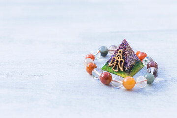 Oragone pyramid with crystal bracelet over blurred background, energy healing and protection with fortune telling tool 