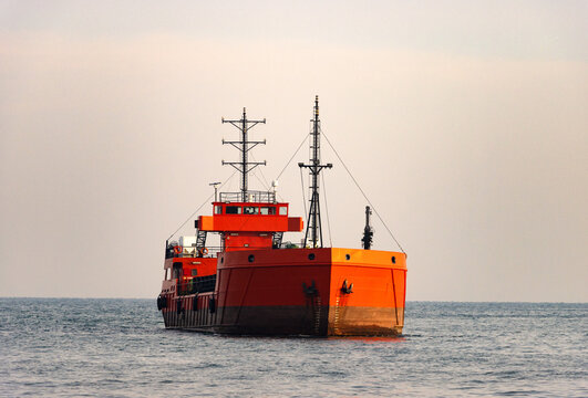 Bright orange cargo vessel with flat bow and two tall masts floating on a calm sea under a pale sky, minimalist maritime scene highlighting industrial design, transportation, and modern shipping.