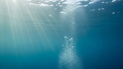 Fototapeta premium Sunlight pierces through the tranquil blue ocean surface, illuminating a steady stream of rising effervescent bubbles in the clear, deep underwater environment