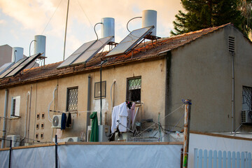 Aging residential house in central Israel with rooftop solar thermal water heaters and tanks on a tiled roof, barred windows, air conditioners and hanging laundry, urban sustainability, solar panels