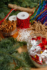 Top view of various Christmas DIY craft materials on a wooden table, including cinnamon sticks, red and white pearl beads, jute twine, and festive tinsel.