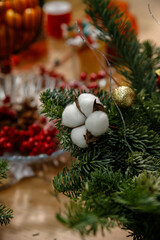 Macro shot of a soft white cotton flower nestled in green fir branches with a golden Christmas bauble and red berries in the background.