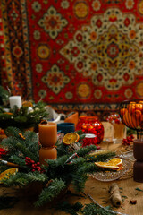 High angle view of a messy creative wooden workspace filled with Christmas decorations, fir branches, candles, and mandarins. Professional florist desk during a DIY holiday wreath making workshop.