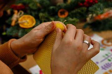 Macro shot of artisan hands carefully rolling a natural honeycomb beeswax sheet into a handmade candle. Detailed process of traditional candle making at a creative holiday workshop.