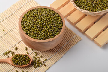 Mung beans in wooden bowls and spoon on bamboo mat background. Healthy organic legumes concept with green pulses, natural food ingredients.