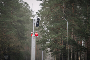 Traffic monitoring camera mounted on a pole in a forested area, surrounded by tall trees and a misty atmosphere, capturing vehicle movement for safety and regulation purposes