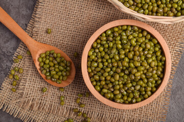 Mung beans in a wooden bowl with a spoon on burlap against a dark stone background. Organic green...