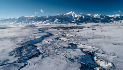 Aerial view of snowcovered landscape with cracked ground and mountains in the background.