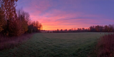 Fototapeta premium Panoramic autumn sunrise painting a rural field and tree line with vibrant orange, pink, and purple sky