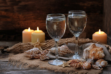 wine glasses, burning candles, seashells on rustic wooden table. beautiful composition of sea vacation theme, romantic beach event dinner. sea vibe decorations for serving festive table. soft focus