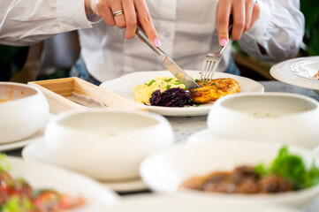 A close-up shot of a person using a knife and fork to cut into a meal of meat, mashed potatoes, and red cabbage in a restaurant setting