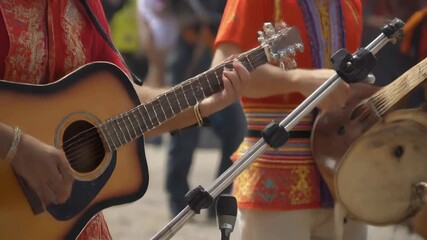 Close-up of hands playing an acoustic guitar and another traditional instrument during a live musical performance.