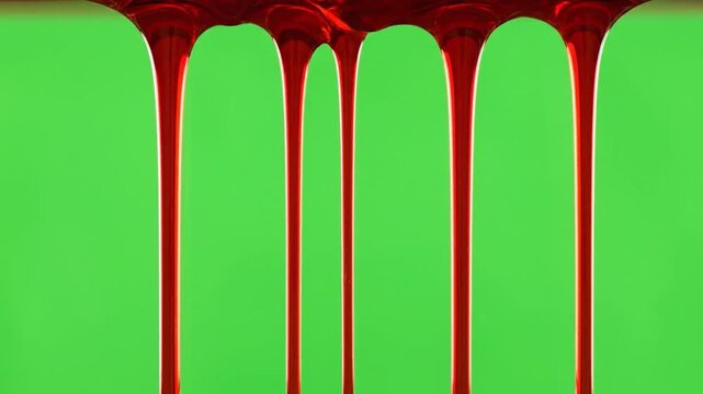 Thick, glossy red liquid drips downwards in several streams against a vibrant green screen