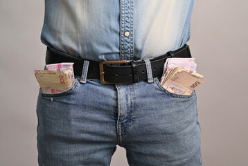 person with denim jeans and belt has bills clearly visible in both pockets, lifestyle of financial success and abundance. man in casual jeans with cash overflowing from his pockets. Ukrainian hryvnia.