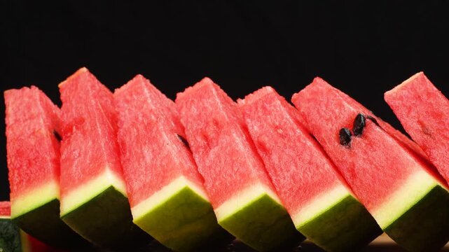 Row of fresh watermelon slices isolated on black background. Juicy red fruit snack close up.