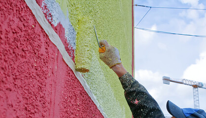 Worker painting a colorful mural on a building wall during the day in an urban setting © Vital