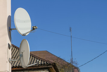 Satellite dishes are mounted on a building against a clear blue sky in an outdoor setting