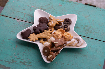 Decorated traditional Christmas gingerbreads arranged on white plate in star shape, various xmas shape cookies