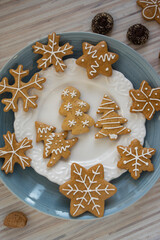 Painted traditional Christmas gingerbreads arranged on blue and white plates on light wooden table, various xmas shapes