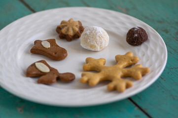 Various traditional Christmas sandbakelse, gingerbread, ball and vanillekipferl on white plates on old vintage painted table