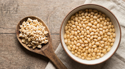 Raw tempeh crumble atop a wooden spoon next to a bowl of soaked soybeans