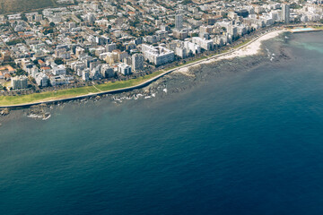 Aerial view of coastal city cityscape next to a calm blue ocean. Urban development by the sea for travel and tourism concept.