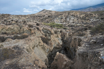 The arid landscape of Tabernas Desert in Almeria, Spain, with rugged hills, sparse vegetation, and rocky outcrops under a cloudy sky. It&rsquo;s a popular filming location