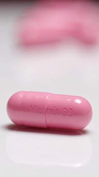 Close-up of a pink capsule with "Vitamin B3" inscription, reflecting on a white surface