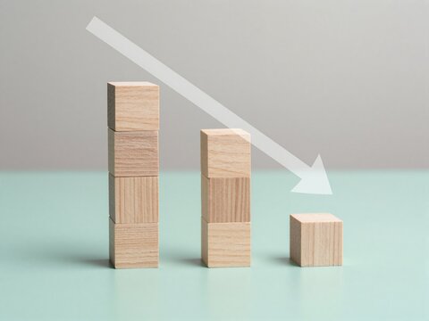 Wooden blocks show declining trend: tall stack drops to single cube, arrow points downward symbolizing decrease or failure.