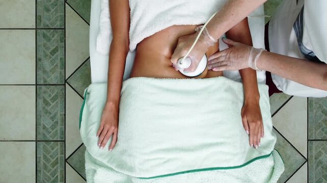 Top view video of a beauty treatment using an ultrasound device applied to the abdomen in a spa or clinic. A professional performs a non invasive body treatment focused on skincare, body contouring. 