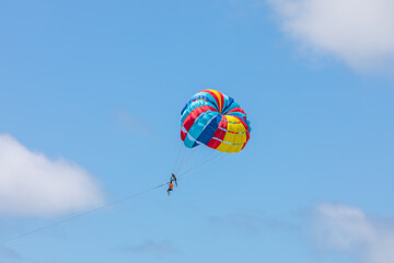 A man in orange life jacket and assistant floating with colorful parachute pulling by long sling.