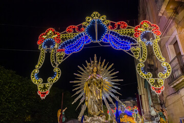 Religious Night Procession With Illuminated Arch, Radiant Virgin Mary Statue, and Decorative Lights