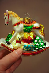 Hand holding a brightly colored holiday ornament featuring a horse, teddy bear, and Christmas elements. Captures the essence of holiday decoration and festive spirit