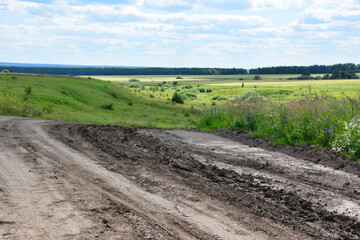 Fototapeta premium Muddy Dirt Road Leading Through Green hills Under a Cloudy Sky with sunlight