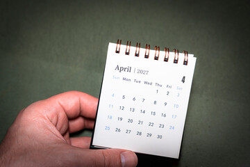 A hand holding a desk calendar displaying the month of April 2027. The visual emphasizes organization and time management, suitable for business, planning, or educational contexts.