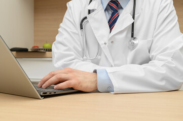 Doctor in a lab coat with a stethoscope sitting at a desk in front of a laptop, telemedicine teleconsultation