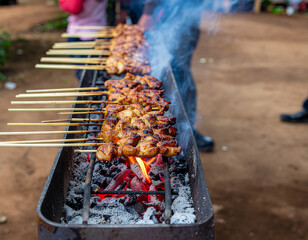 Chicken satay skewers grilling over hot coals with smoke rising at an outdoor food stall.