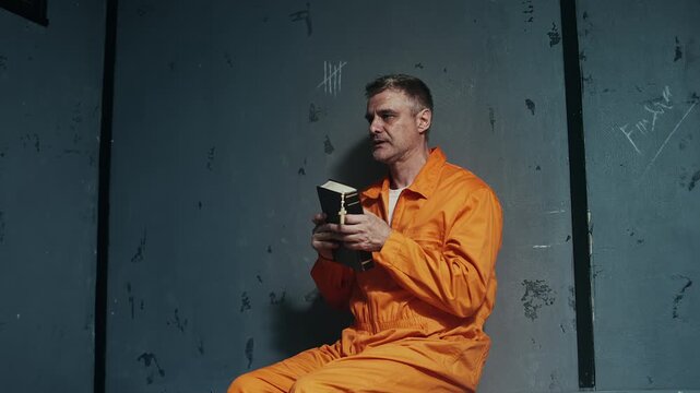 Convicted man in orange prison robe reading Bible in cell, seeking forgiveness