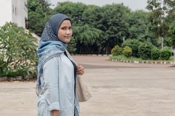A young Indonesian Muslim woman carrying a women's shoulder bag while walking outdoors