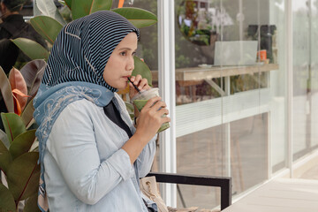 A young Indonesian Muslim woman enjoying her iced matcha drink at a coffee shop