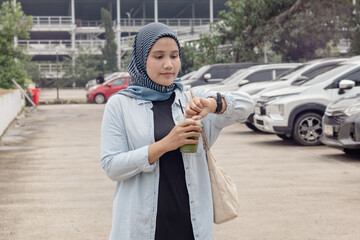 A young Indonesian Muslim woman checking the time on her watch while walking in the parking lot