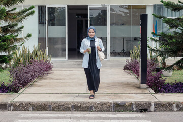 A young Indonesian Muslim woman crossing the street while carrying her drink