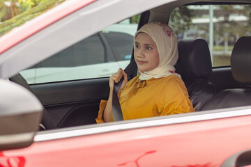 A young Indonesian Muslim woman fastening her seat belt before driving