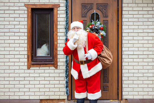 Santa Claus stands near the front door. He puts his finger to his mouth, calling for silence.