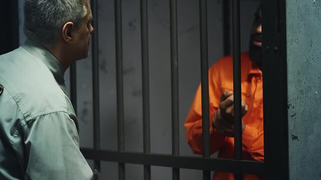 Strict prison guard placing male criminal into cell, removing handcuffs