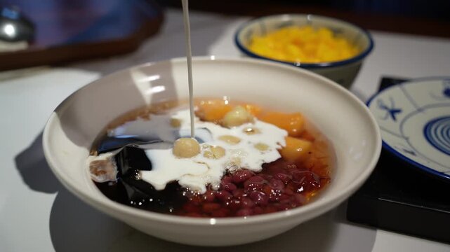Pouring Milk into Bowl of Cantonese Sweet Soup with Assorted Ingredients
